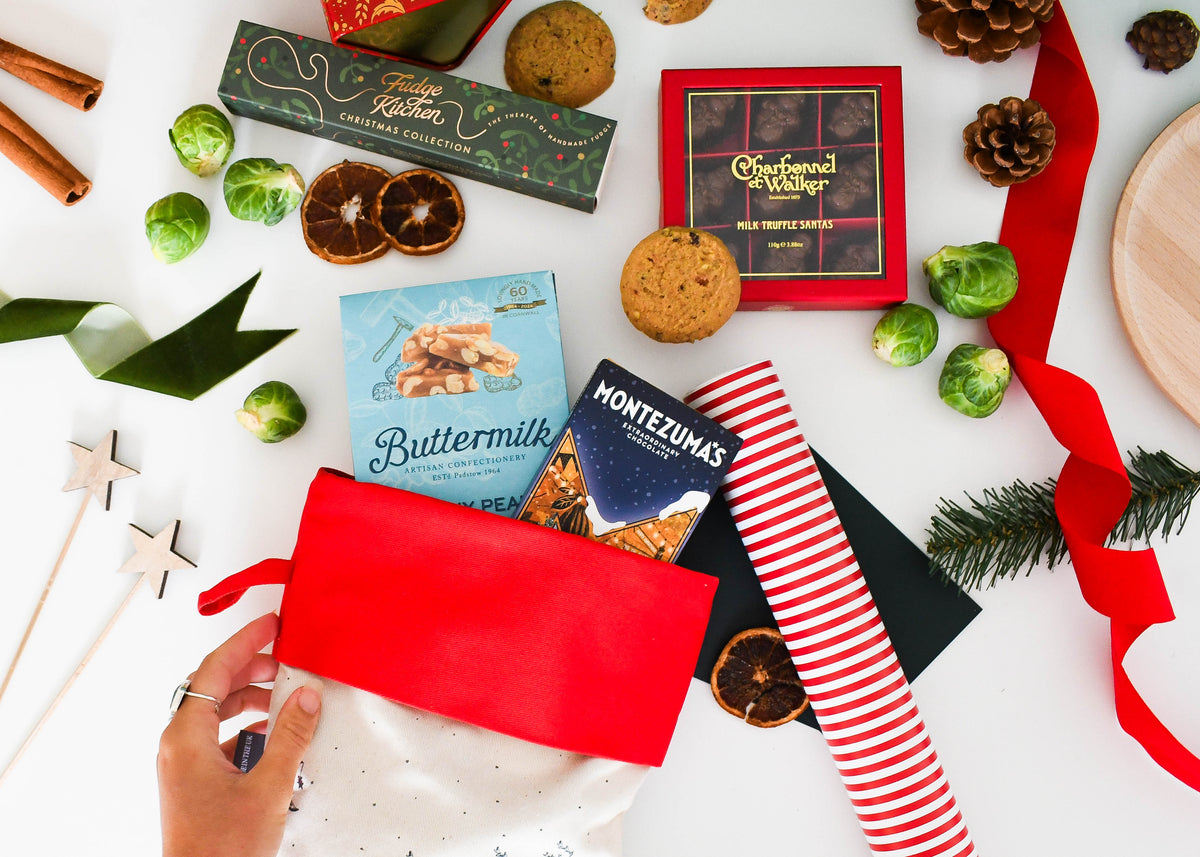 Hand lifting the red cuff of the stocking, with Montezuma's, Buttermilk and Charbonnel et Walker chocolates around it