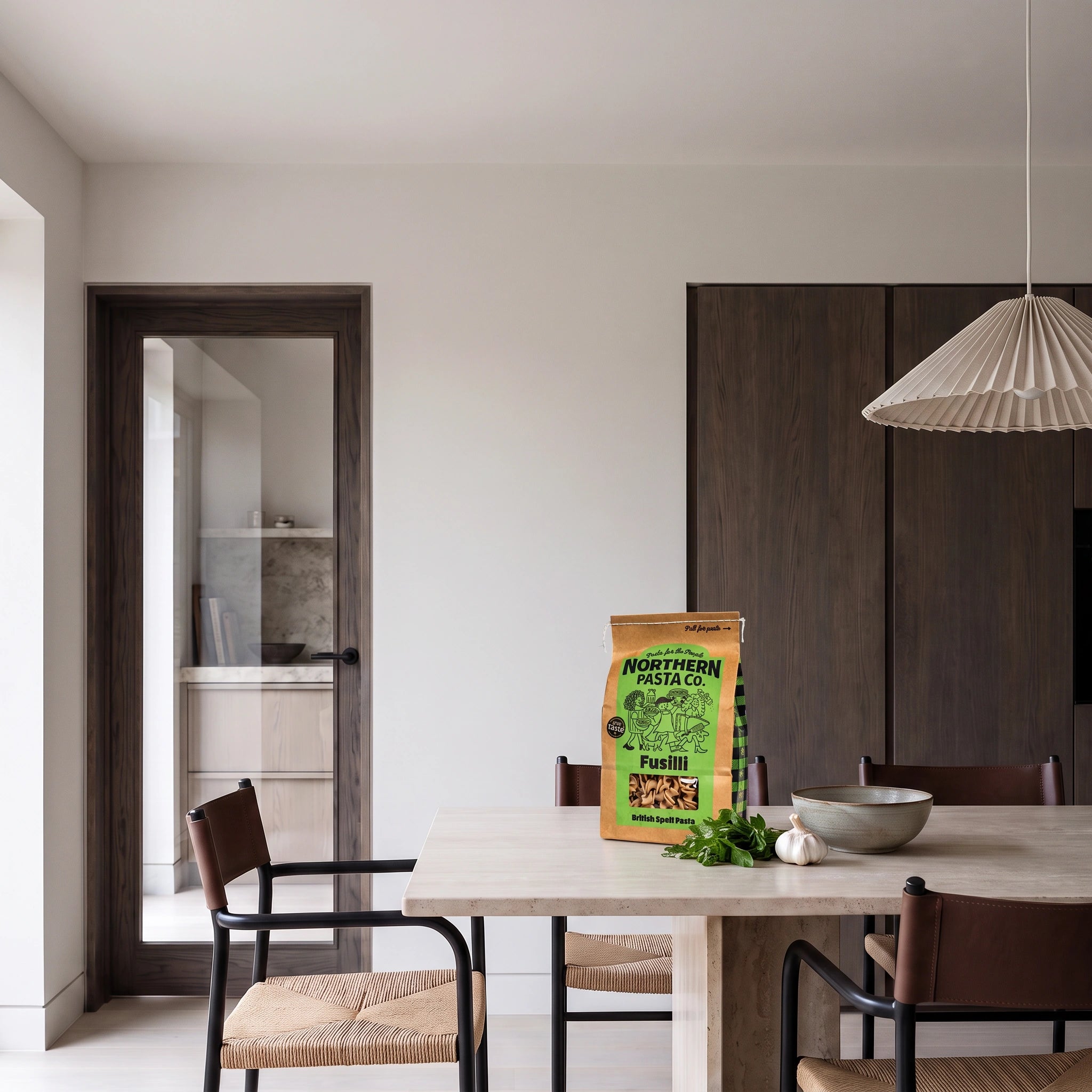 Northern Pasta Co. British Spelt Fusilli bag on a minimalist stone dining table with fresh herbs and garlic