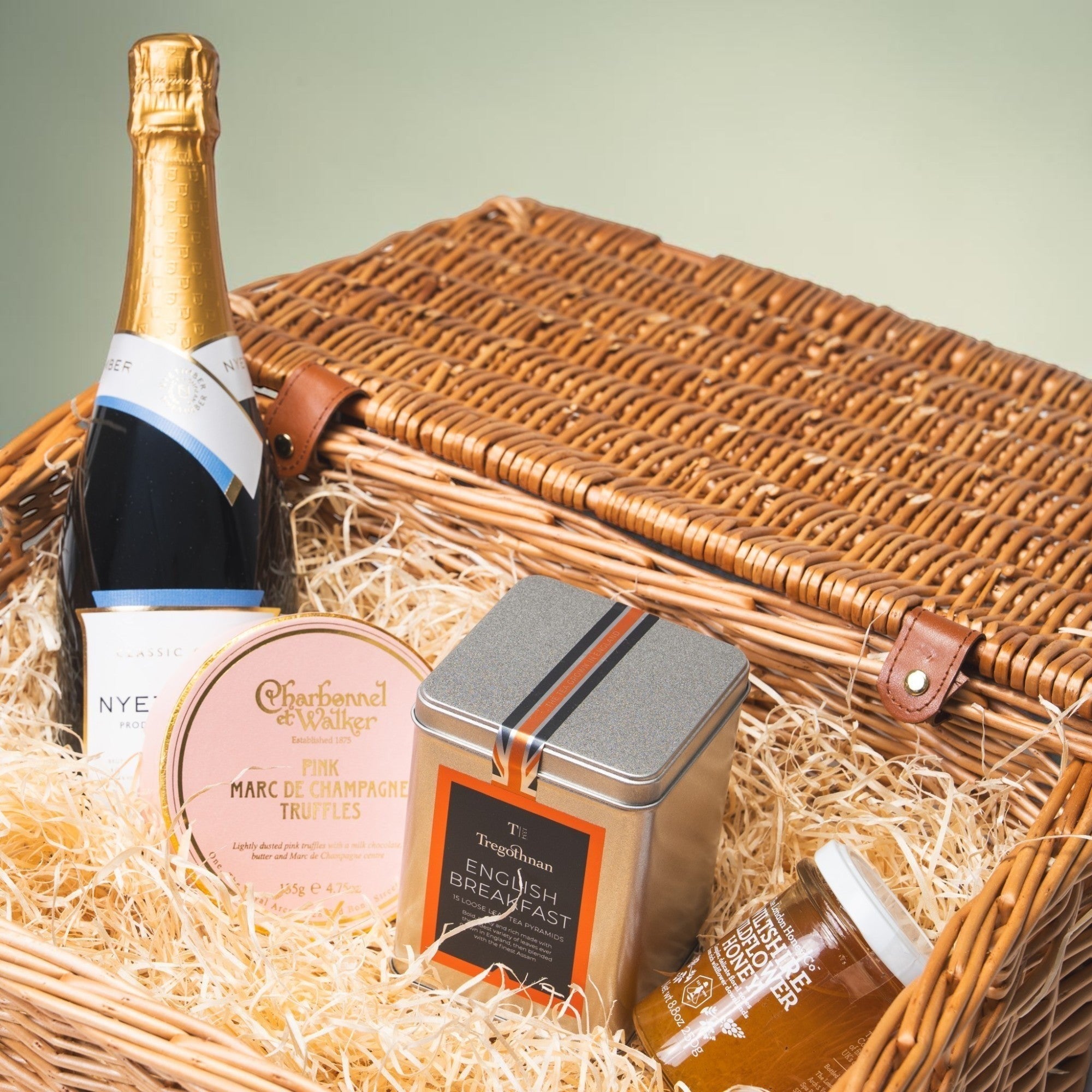 Made In England luxury picnic hamper with sparkling wine, pink champagne truffles, English breakfast tea, and wild honey in a wicker basket.