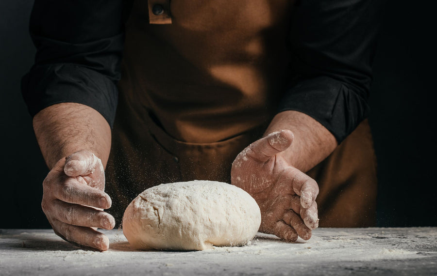 A baker shaping a loaf on a floured bench