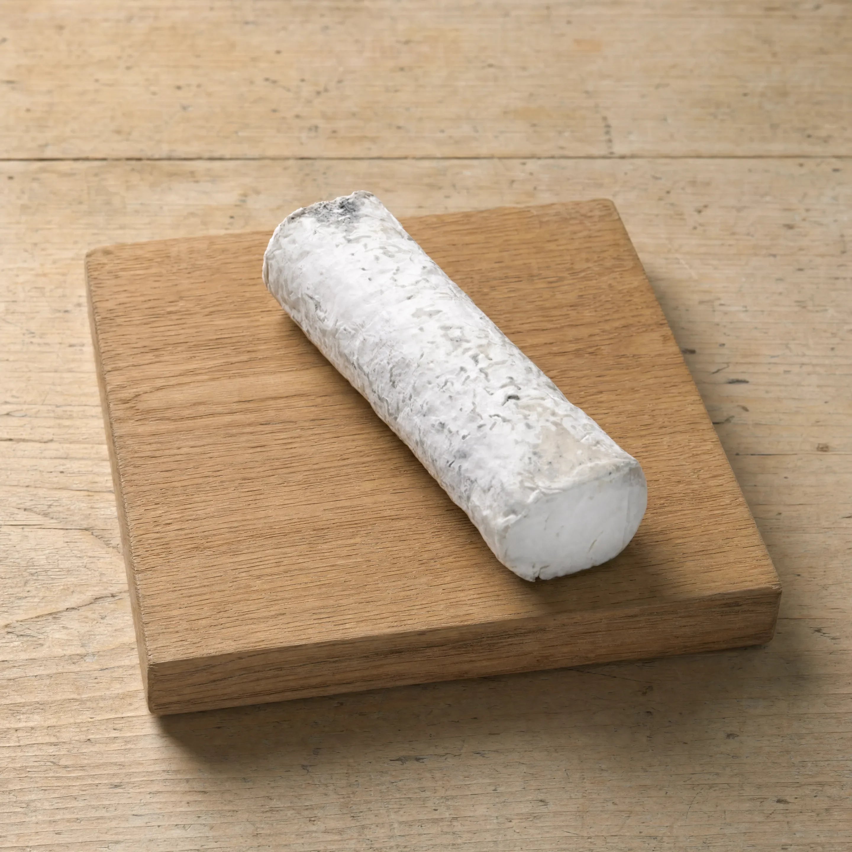 Golden Cross ashed goats' cheese log on an oak board, English cheesemonger counter