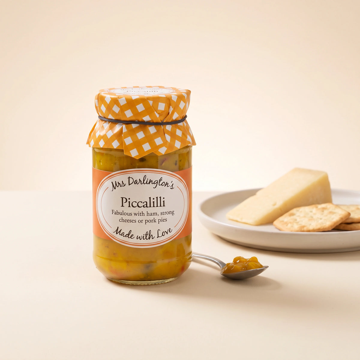 Mrs Darlington's Piccalilli jar on a pale table with a plate of hard cheese and crackers and a spoonful of piccalilli