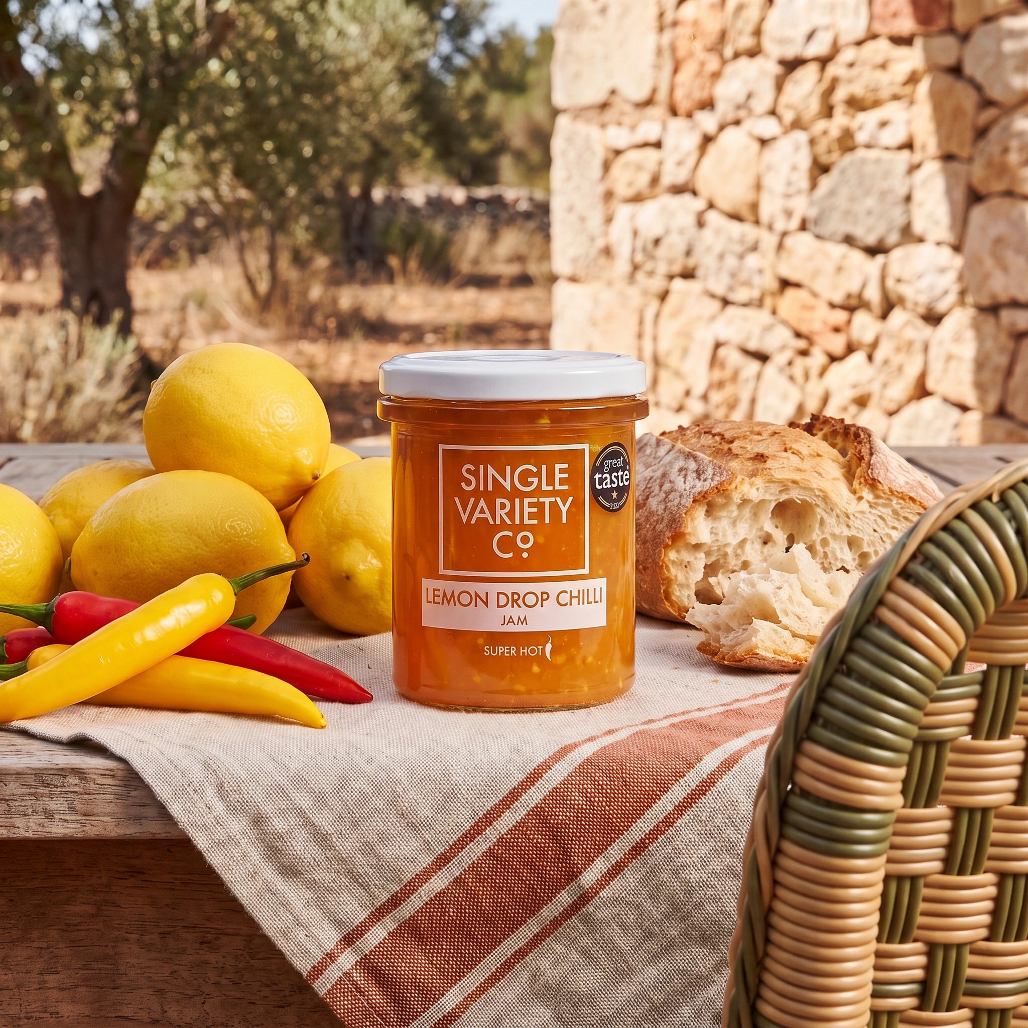 Single Variety Co. Lemon Drop Chilli Jam jar on a sunlit patio table in an olive grove with lemons and chillies