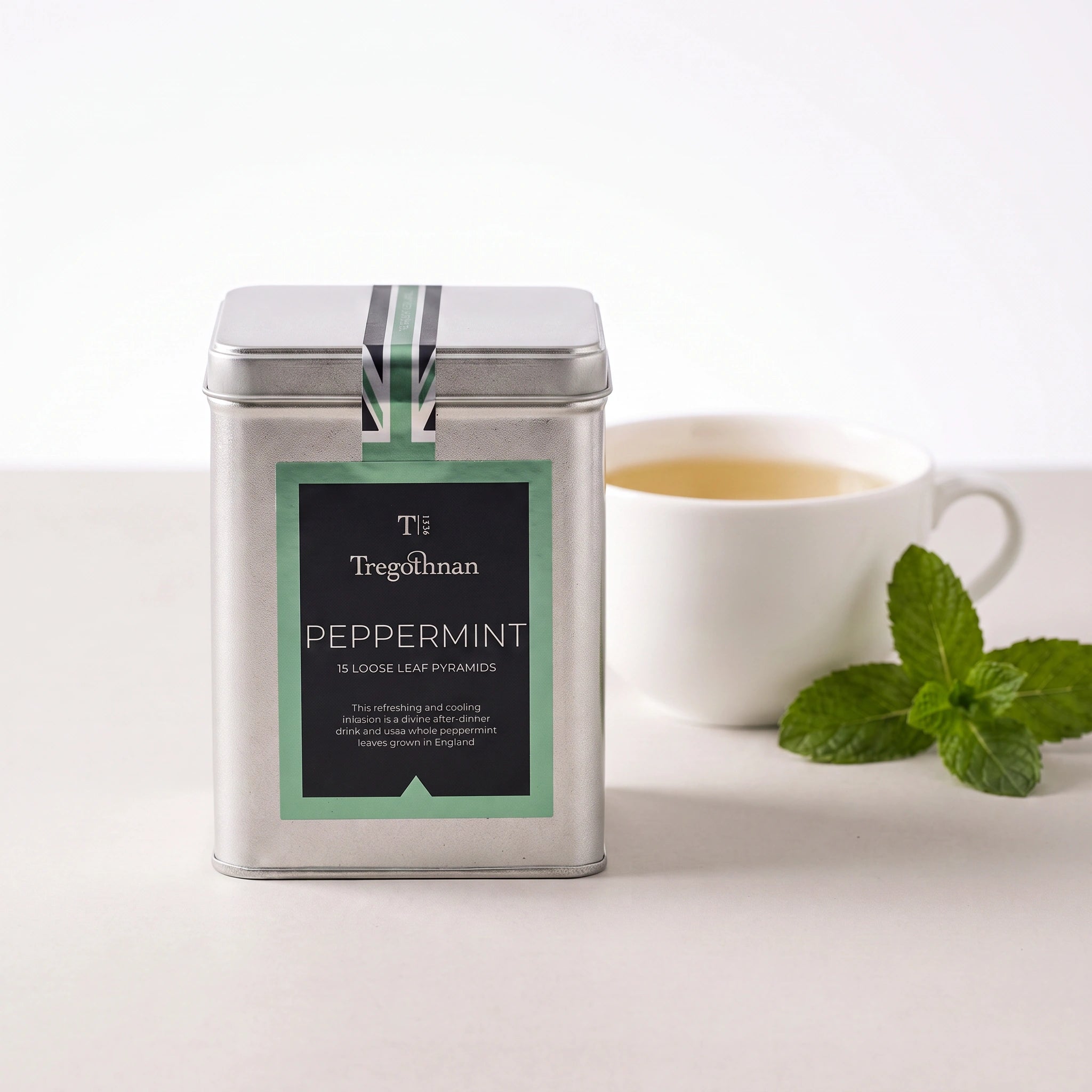 Tregothnan Peppermint tea tin front-on with a cup of tea and mint