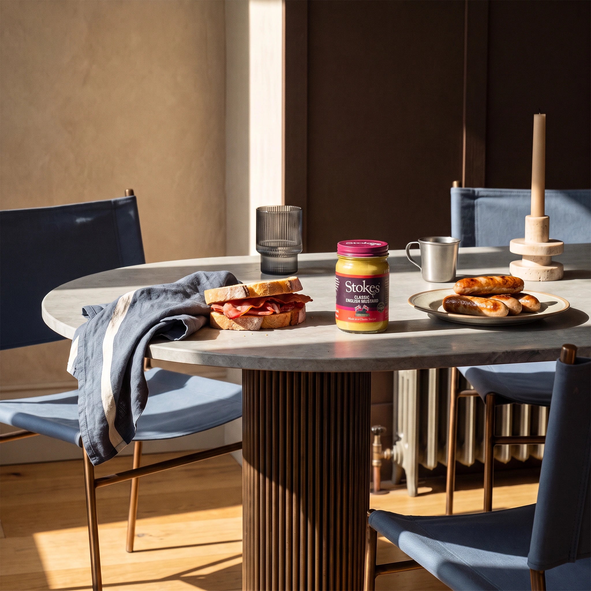 Stokes Classic English Mustard jar on a sunlit dining table with a bacon sandwich and sausages