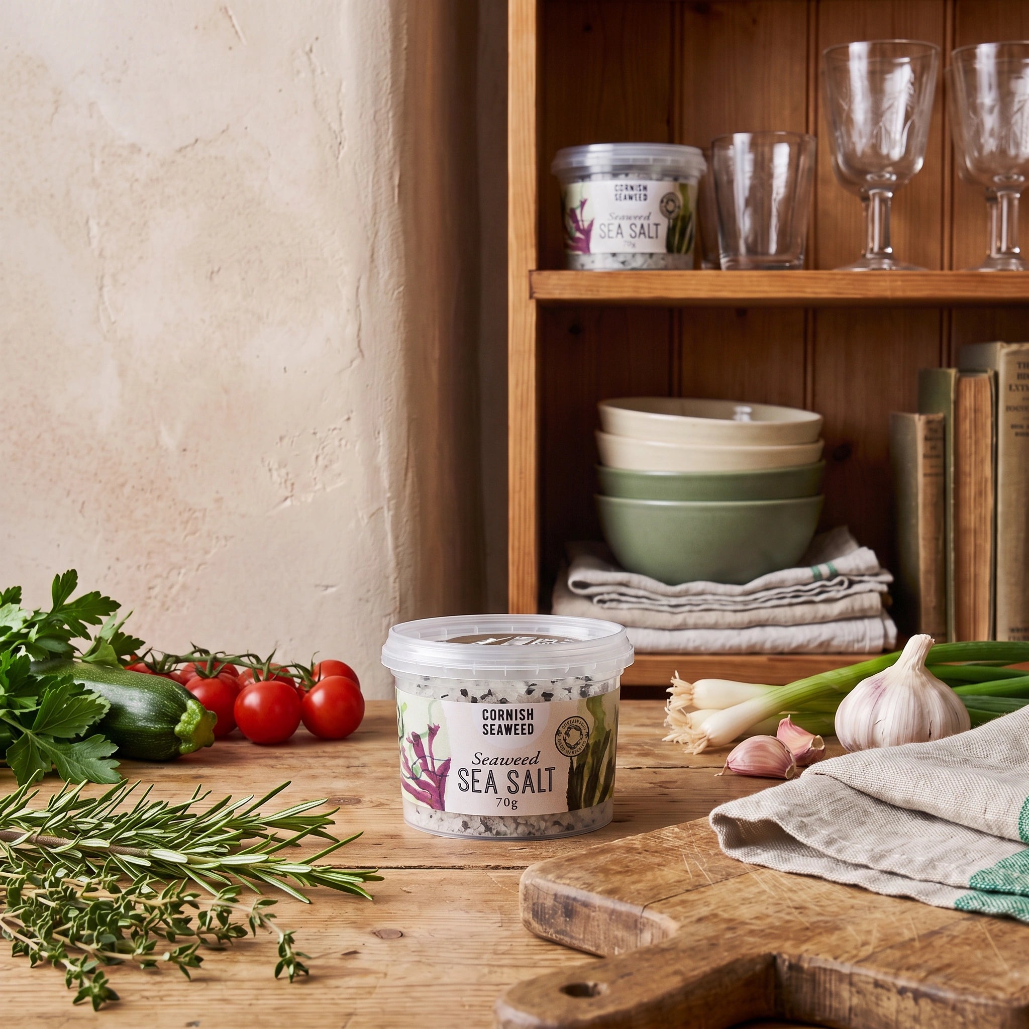 Cornish Seaweed Sea Salt jar in a rustic kitchen setting with fresh vegetables and herbs