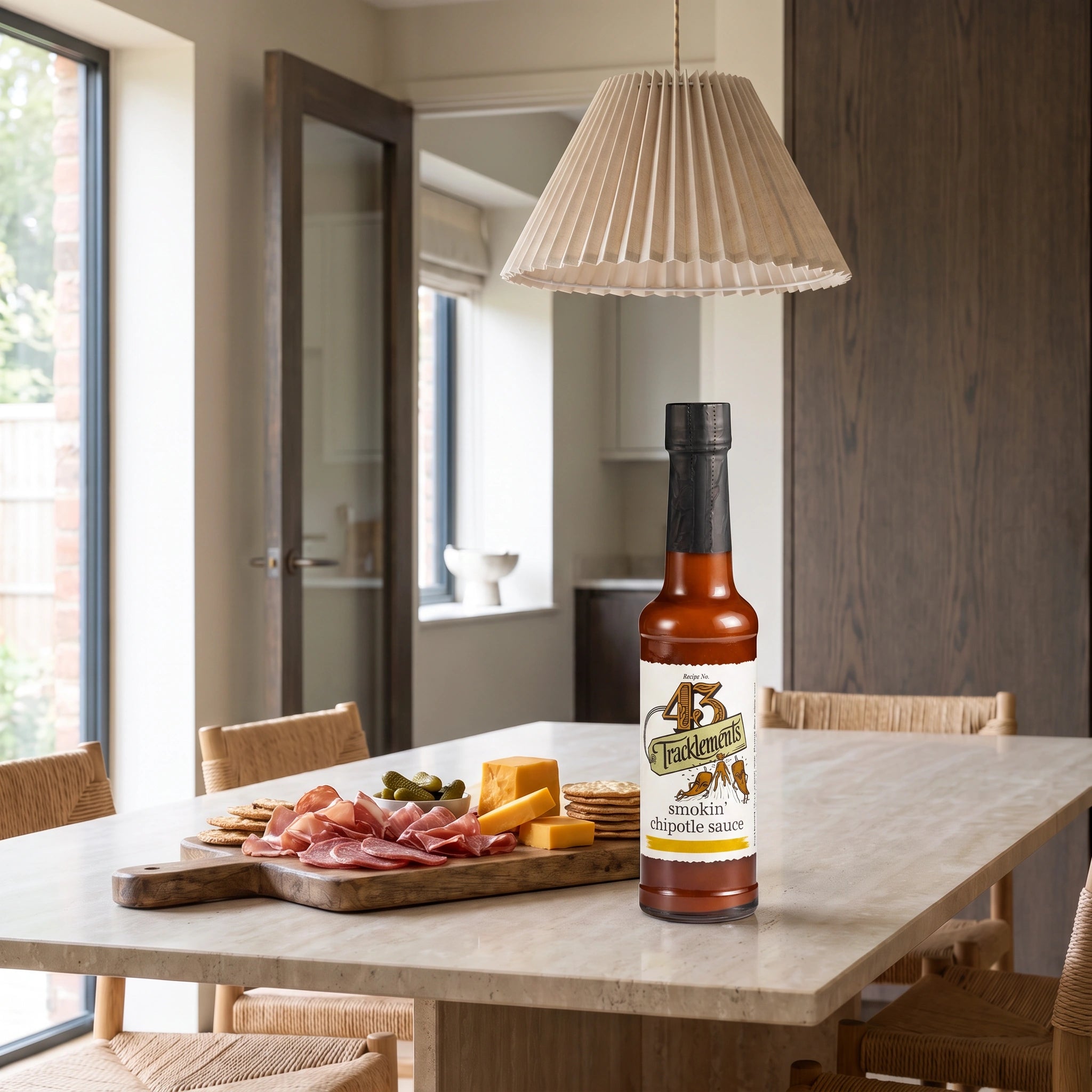 Tracklements Smokin' Chipotle Sauce bottle on a minimalist stone dining table with a charcuterie board