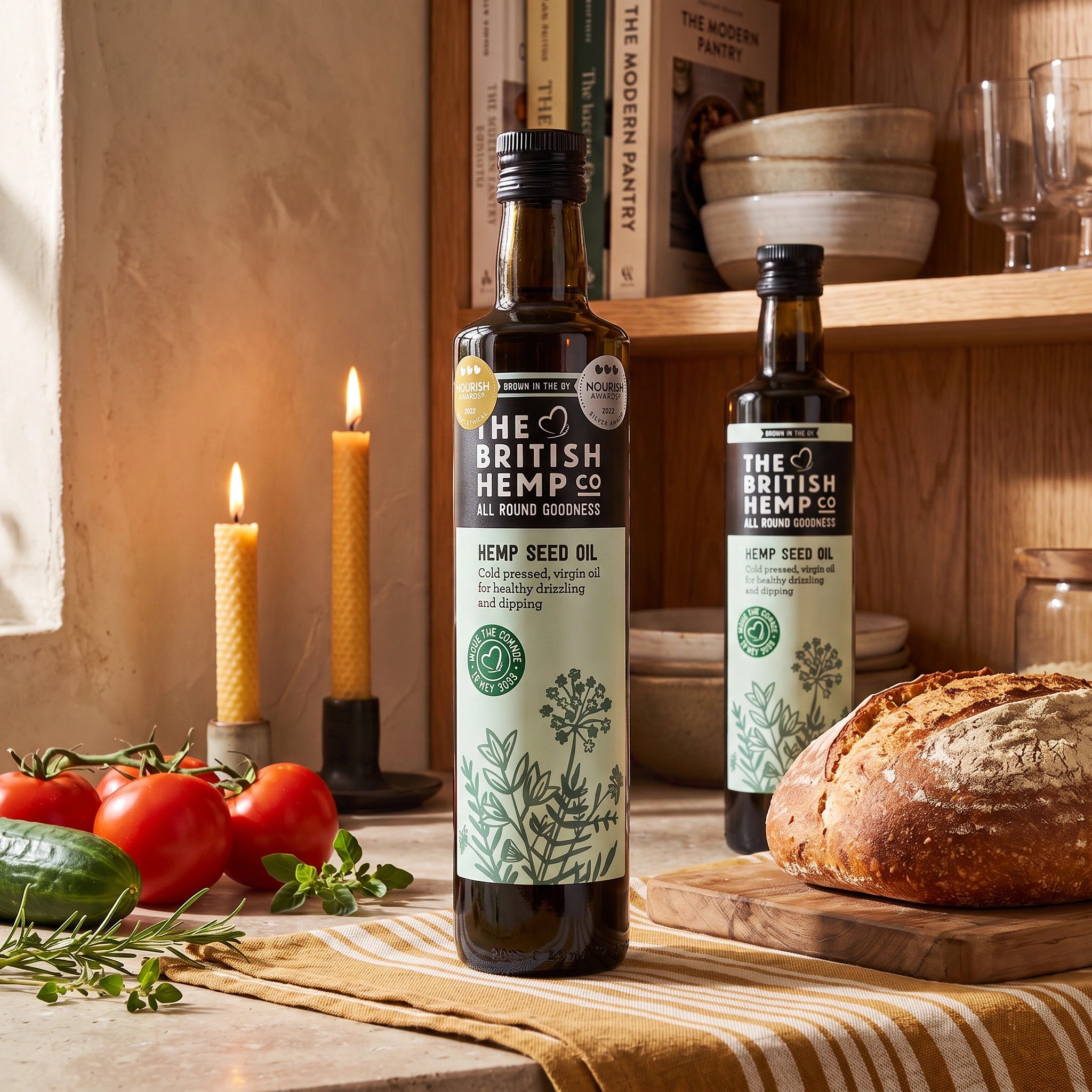 The British Hemp Co. Cold Pressed Hemp Seed Oil bottle in a rustic kitchen with bread, tomatoes and cucumber