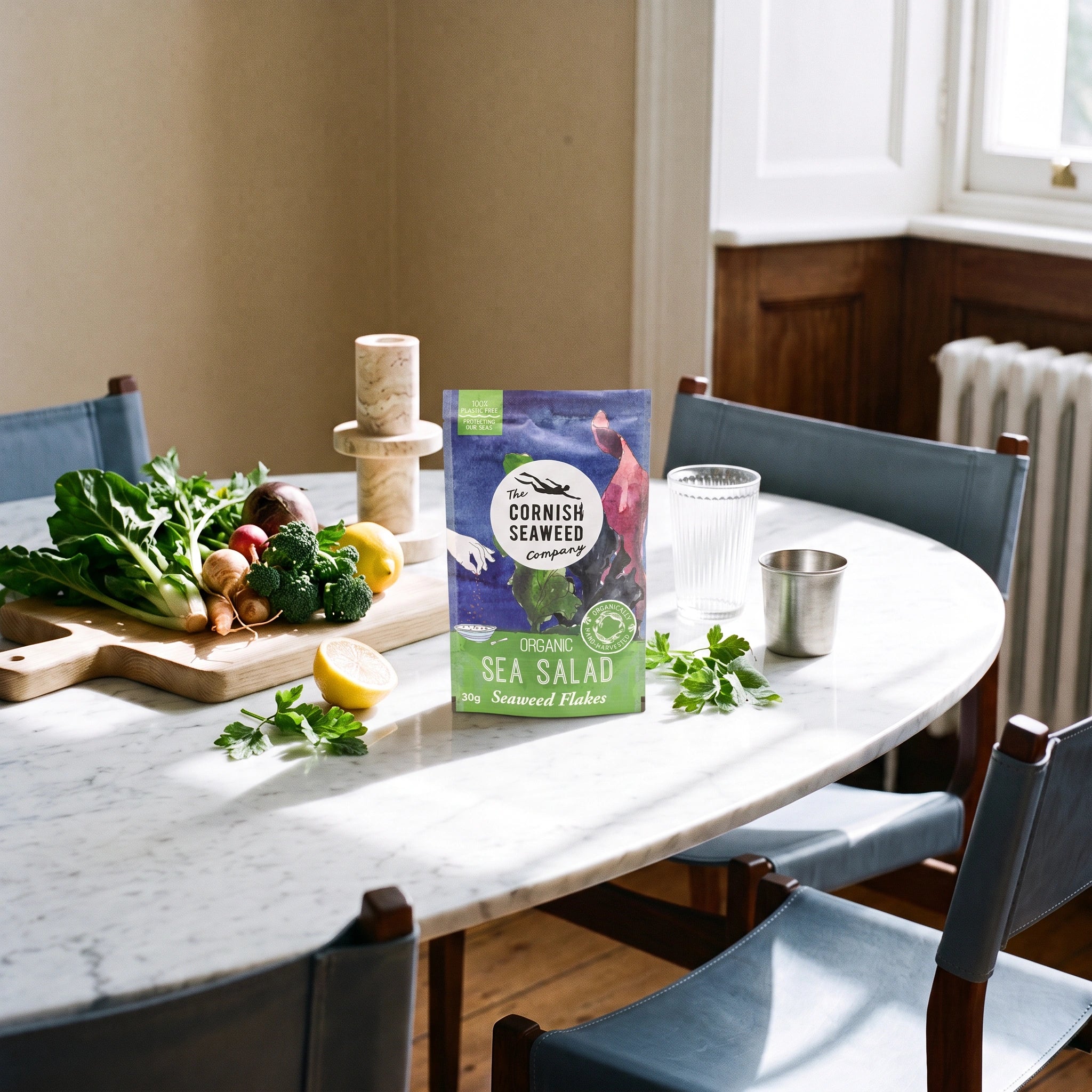 The Cornish Seaweed Company Organic Sea Salad Flakes pouch in a sunlit marble dining setting with fresh vegetables