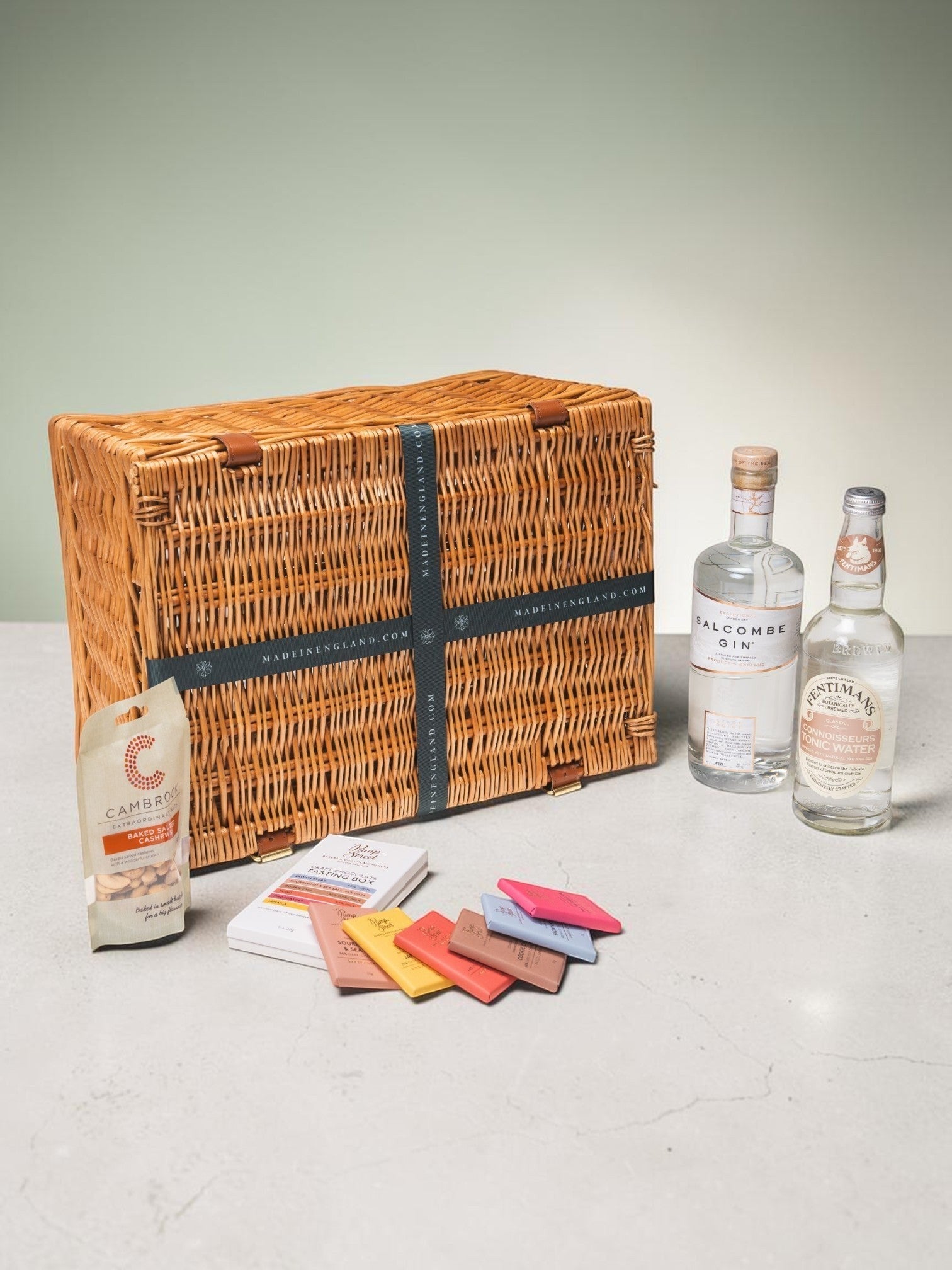 Made In England Gin And Tonic Hamper with Salcombe Gin, Fentimans Tonic, cashews, and Pump Street chocolate bars in a wicker basket.