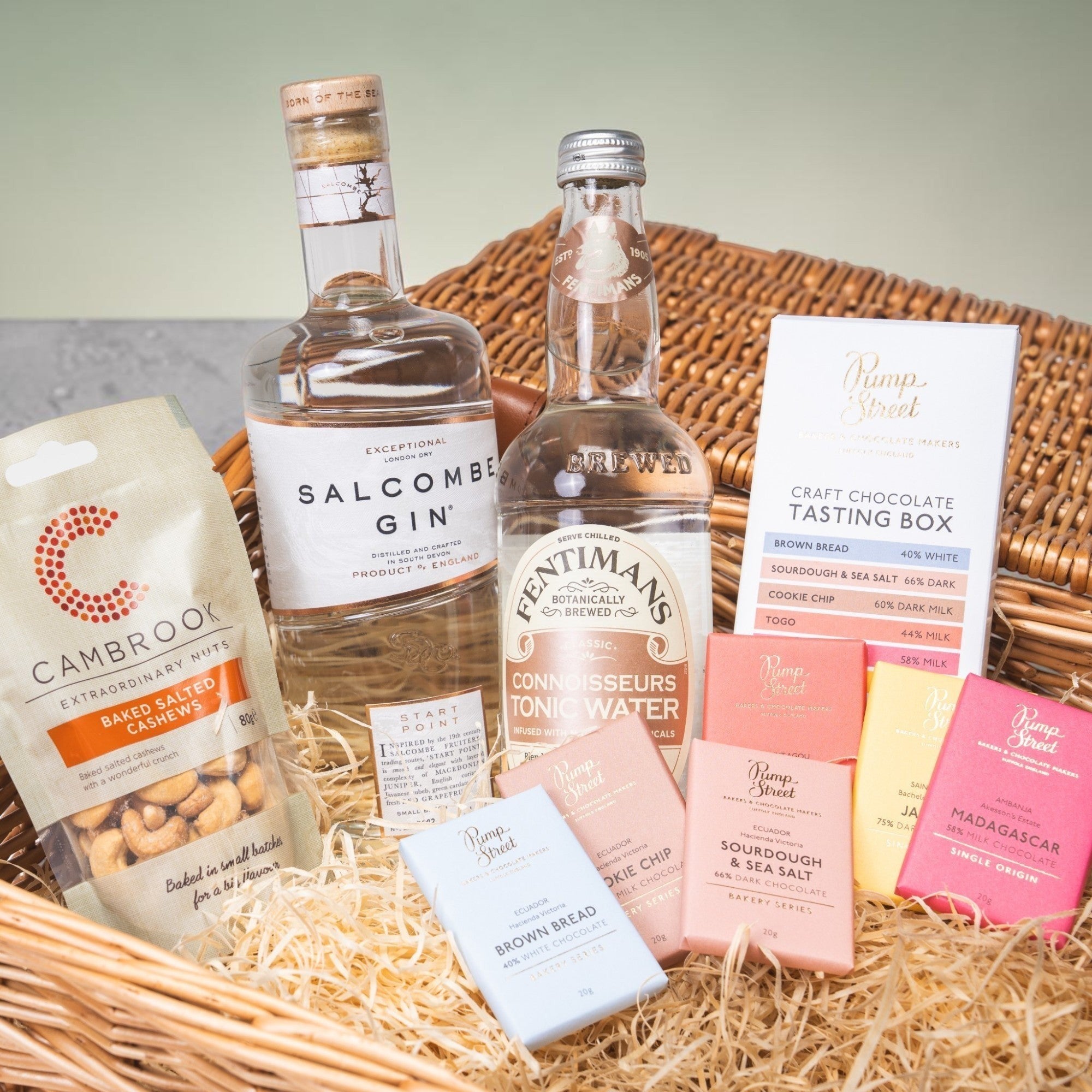 Made In England Gin And Tonic Hamper with Salcombe Gin, Fentimans Tonic, cashews, and Pump Street chocolate bars in a wicker basket.