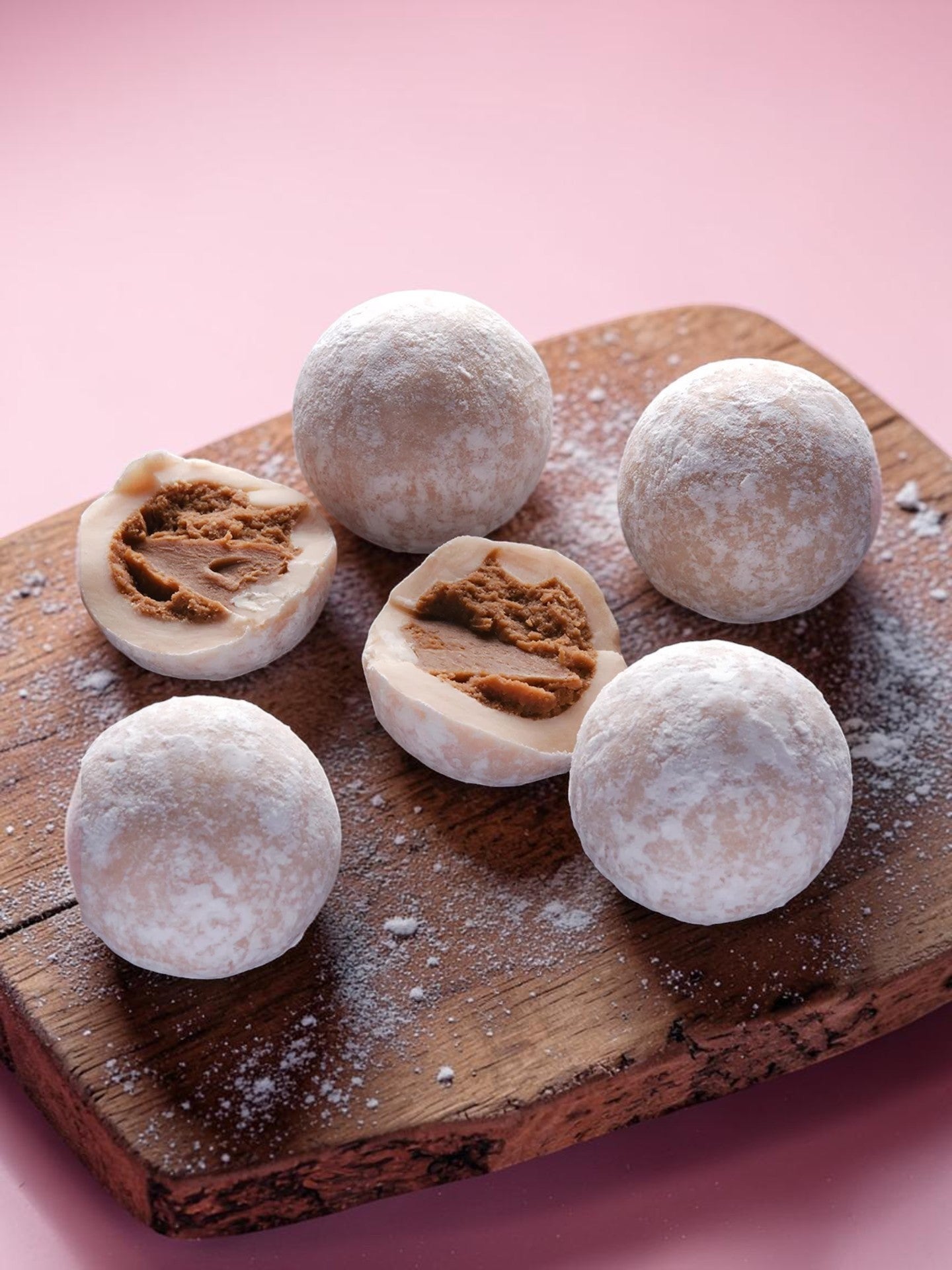 Made In England Pink Marc De Champagne Truffles, dusted white, on a wooden board with a pink background.